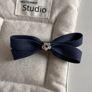Denim bow hair clip detail view, showcasing dark blue fabric texture and a cute silver flower charm.