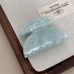 Detail close-up of a light blue translucent acetate hair claw clip embellished with stones.
