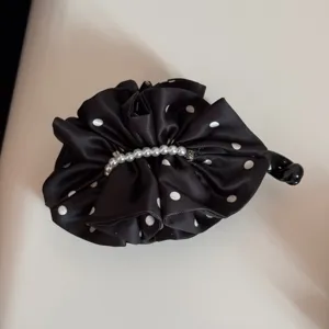 Primer plano de la pinza de pelo de satén con lunares negros, pliegues delicados y detalles de perlas.