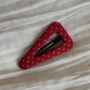 Close-up detail of red polka dot fabric hair clip showing texture and vibrant color pattern.