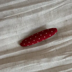 Red fabric polka dot hair clip detail, cute sweet hair accessory closeup shot.