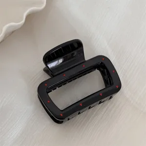 Vue en detail d'une pince a cheveux rectangulaire noire elegante avec des pois rouges.