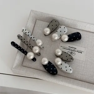 Close-up detail of chic black and white polka dot hair clips featuring large pearls.