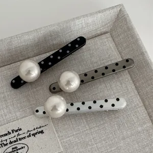 Close-up detail of three elegant polka dot hair clips adorned with large pearls on a linen tray.