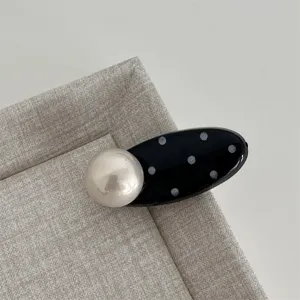 Close-up detail of sweet black and white polka dot oval hair clip with large pearl decor.