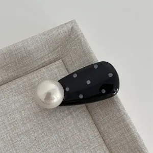 Detailed view of cute black white polka dot pearl hair clip, stylish oval side accessory.