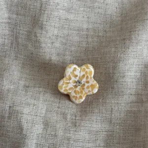 Primo piano di una mini molletta per capelli a fiore giallo con strass centrale luminoso.
