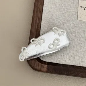 Close-up detail of silver leather hair clip featuring elegant white pearl bow design.
