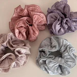 Detail view of large ruffled fabric scrunchies in four soft pastel colors for hair styling.