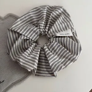 Close-up detail of striped fabric hair scrunchie with handmade tag on clean white table.