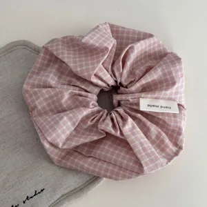 Close-up detail of a pink plaid fabric hair scrunchie showing soft texture and handmade label.
