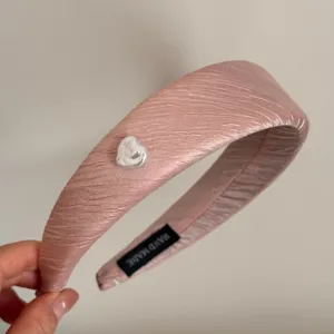 Detailed view of a pink pleated headband with a cute heart charm and handmade inner label.