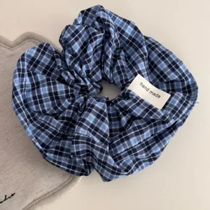 Detail shot of blue plaid fabric hair scrunchie with handmade label on cozy table surface.