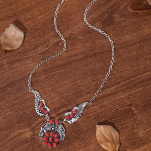 Detailopname van boheemse vintage zilverkleurige vleugel ketting met rode stenen op hout.