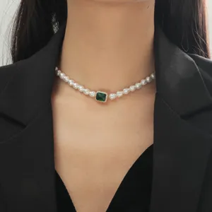 Vista dettagliata di una collana girocollo di perle retrò con una pietra preziosa verde centrale.