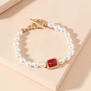 Primo piano di bracciale di perle vintage con chiusura dorata e gemma rossa centrale.
