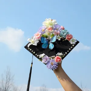 Handmade floral graduation cap with colorful artificial flowers, blue butterfly and pearls for ceremony.
