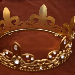 Close-up detail shot of a vintage gold crown headpiece showcasing intricate metalwork and rhinestone details on brown fabric.
