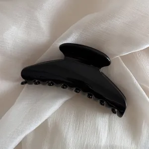 Black hair claw clip detail showing smooth glossy finish and sturdy teeth design for styling.