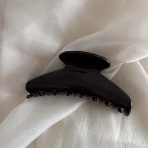 Close up of a dark minimalist hair claw clip on soft white fabric, elegant daily hair accessory.