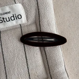 Detailed close-up of a dark brown velvet BB hair clip on textured striped fabric, elegant and simple style.