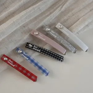 Vue détaillée de pinces à cheveux à carreaux et paillettes avec strass en cœur et texte.