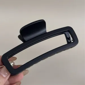 Gros plan détaillé d'une pince à cheveux rectangulaire noire mate à la texture soignée.