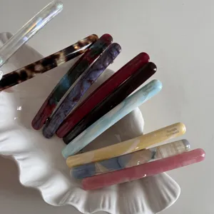 Vue détaillée de pinces à cheveux fines en acétate coloré disposées sur une assiette en coquillage.