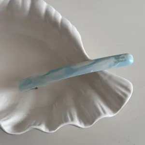 Gros plan détail d'une barrette à cheveux acétate marbrée bleue blanche sur coquillage.