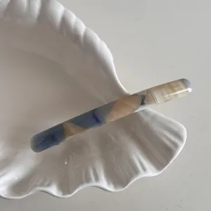 Vue détaillée d'une pince à cheveux fine en acétate avec un motif marbré bleu et beige.