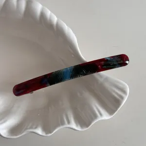 Gros plan détaillé d'une barrette à cheveux acétate marbrée sur un plat coquillage blanc.