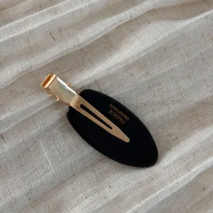 Close-up view of the elegant black and gold oval hair clip featuring a secure duckbill design.