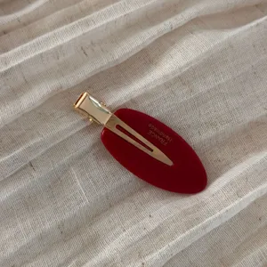 Close-up detail of the elegant red oval hair clip with gold metal accent and textured finish.