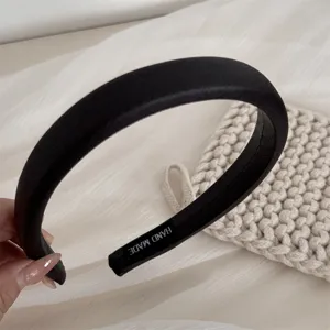 Detailed shot of a black wide fabric headband featuring soft material and handmade label.