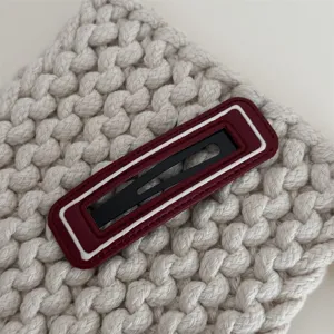 Close-up detail van de stijlvolle leren haarklem met witte rand op gebreide stoftextuur.