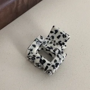 Close-up detail of a mini acetate hair claw clip with a chic black and white pattern.