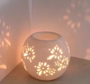 Detalle de lampara de aroma de vela de ceramica con patron floral y luz calida y suave.