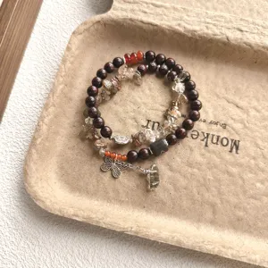 Vue détaillée du bracelet rétro à double tour en perles de bois et cristaux avec un charm papillon.
