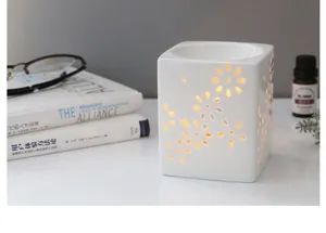 Détail d'un diffuseur d'arôme en céramique blanche avec motif floral ajouré et douce lumière.