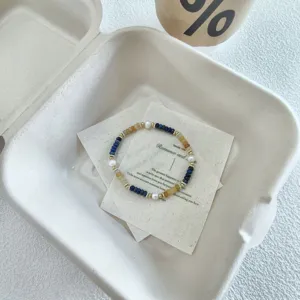 Primo piano dettaglio di un braccialetto impilabile di pietre preziose e perle su cartoncino.