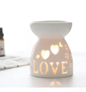 Detail view of the white ceramic aroma lamp featuring hollow hearts and warm glowing LOVE text.