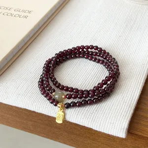 Détail de bracelet en grenat multi-tours avec perle de jade et pendentif de bénédiction.