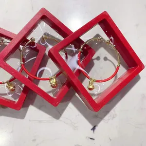 Gros plan d'un bracelet en corde tressée rouge avec cloche dorée dans une boîte de présentation.