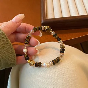 Détail du bracelet de perles en œil de tigre et cristal avec pierre naturelle et gourde dorée.