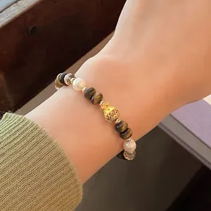 Gros plan détaillé du bracelet en perles d'œil de tigre avec un charm gourde doré.