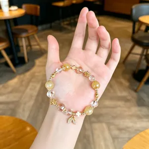 Close-up detail of a crystal beaded bracelet with golden leaf pendant and clover charms on hand.