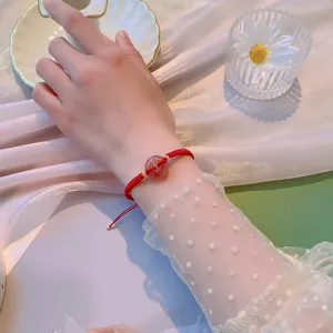 Bracelet en cordon rouge tissé à la main avec perle de cristal de fraise et détails dorés.