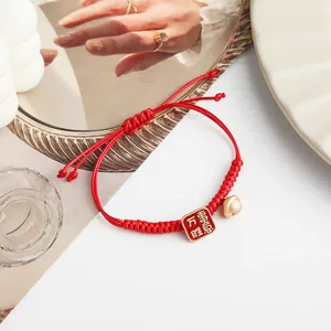Rotes geflochtenes Armband mit Gluecksanhaenger und kleiner Glocke, traditioneller Neujahrsschmuck.