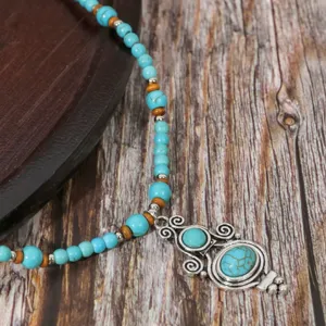 Turquoise beaded necklace detail shot with vintage silver pendant on rustic wooden background.