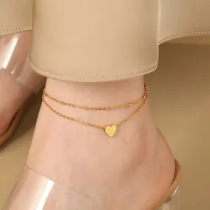 Close-up detail of a double-layered gold anklet with a cute heart pendant, worn gracefully.